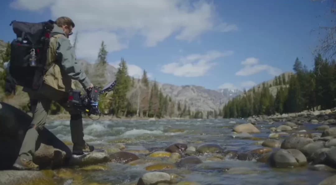 A hiker wearing a DNSYS Z1 steps across rocks beside a mountain stream.