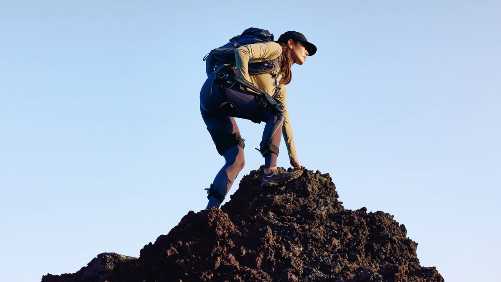 A hiker wearing Hypershell Halo and a backpack climbs over rocky ground.