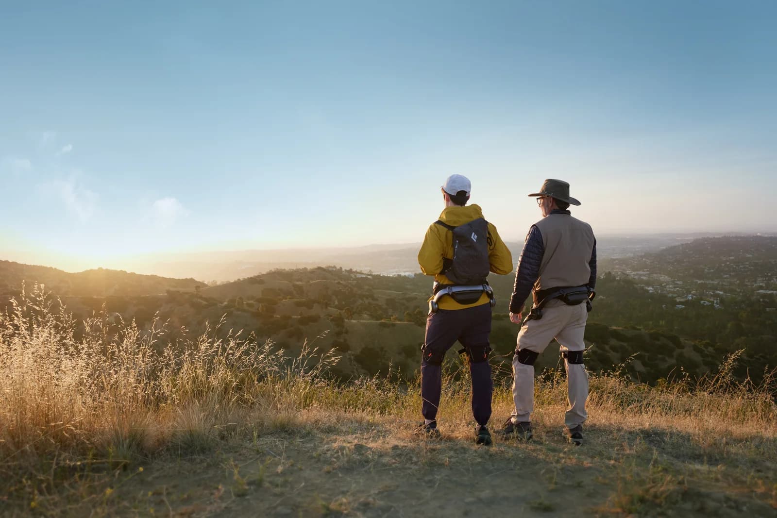 Two people wearing Hypershell hip exoskeletons on a hillside at sunset.