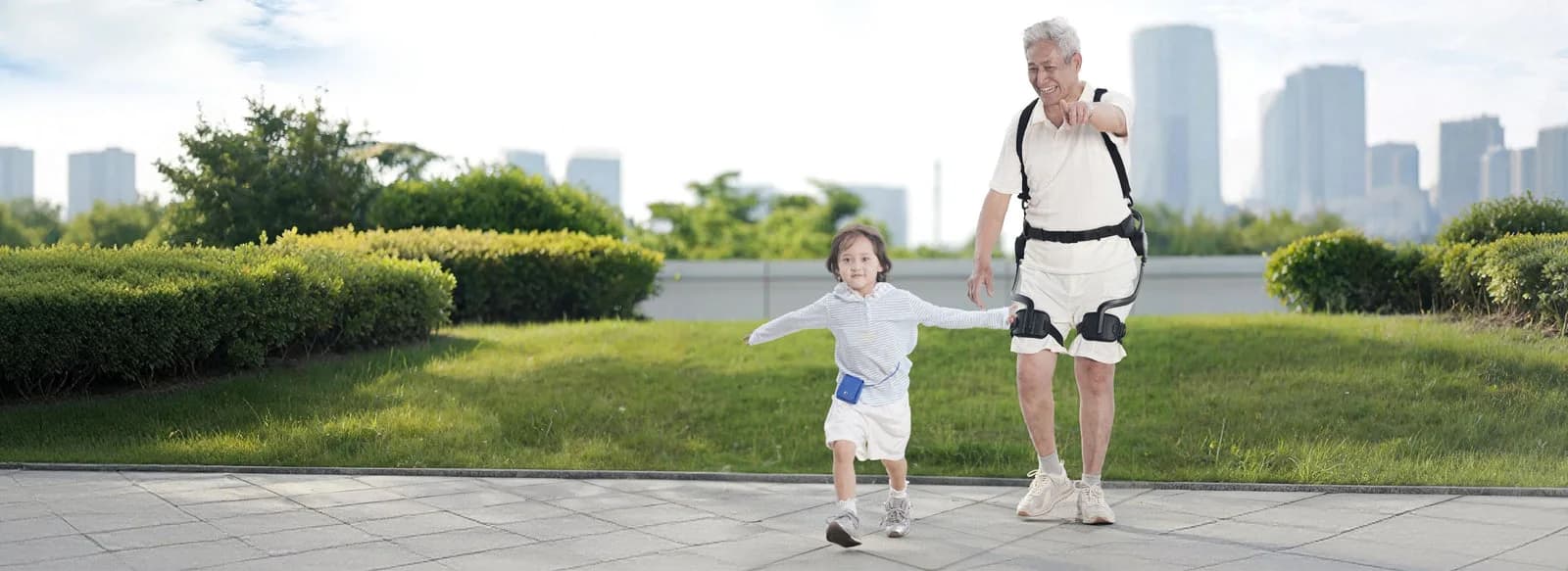 An adult wearing a RoboCT hip exoskeleton walks beside a child on a paved path.